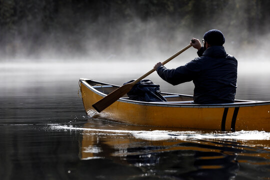 Focused man paddles canoe into fog on a tranquil lake