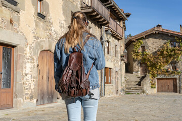 Stylish young girl walking with fashion jeans jacket and backpack in old medieval village.