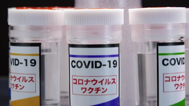 CORONAVIRUS (COVID-19) VACCINE close up shot. Colorful glass bottle of liquid remedy for injection use. Manufacture drugs for medical supplies of pharmacy industry. Label in Japanese language.