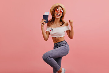 Obraz premium Slender beautiful girl jumps and dances from happiness, rejoicing at accomplished trip abroad. Studio photo of pretty woman laughing in pink round glasses