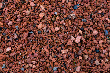 Ground texture with small multi-colored stones. Pebbles of red and terracotta color. Stone decoration of sidewalks and footpaths in parks, squares and courtyards. Perfect for background and design.