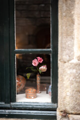 Three roses in a vase by the window of a rustic home.