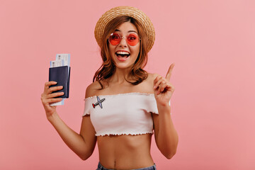 Young woman in great mood remembered that she had to go to airport. Portrait of attractive brown-haired woman in pink glasses posing with documents