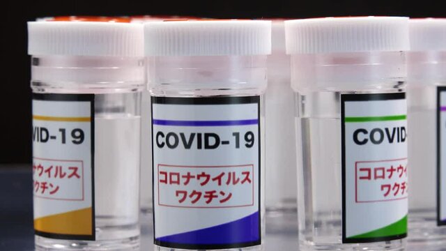 CORONAVIRUS (COVID-19) VACCINE close up shot. Colorful glass bottle of liquid remedy for injection use. Manufacture drugs for medical supplies of pharmacy industry. Label in Japanese language.