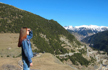 Naklejka premium A girl with red hair looks at the mountain's landscape against the bright blue sky. Travel content