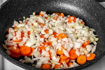 Vegetables are fried in a pan on the stove. Finely chopped onions and carrots are stewed in a pan. The food is cooked in the home kitchen. 
