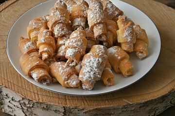 cottage cheese bagels in powdered sugar lie on a white plate side view on a wooden round section of birch