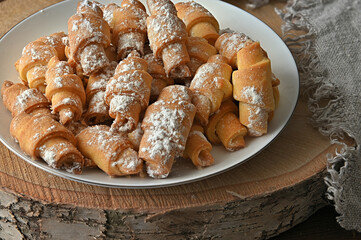 cottage cheese bagels in powdered sugar lie on a white plate side view on a wooden round section of birch on the right the edge of a linen cloth