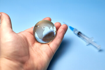 A man holds in his hand a glass globe the planet earth, a syringe in the background.