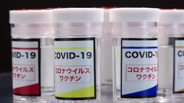 CORONAVIRUS (COVID-19) VACCINE close up shot. Colorful glass bottle of liquid remedy for injection use. Manufacture drugs for medical supplies of pharmacy industry. Label in Japanese language.