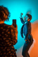 Party lifestyle, a young woman records a video of a young man dancing at a party with orange and blue lights