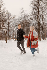 Fototapeta na wymiar Young romantic couple is having fun outdoors in winter. Two lovers are hugging and kissing in Saint Valentine's Day. Hipster couple hugging each other in winter forest. Love story.
