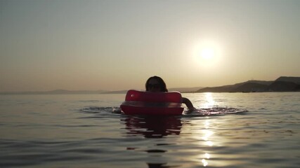 Middle shot of girl lying and swimming on the inflatable mattress in the evening sea. Woman lying and swimming on the inflatable mattress in the sea. Khalkidhiki, Greece High quality FullHD footage