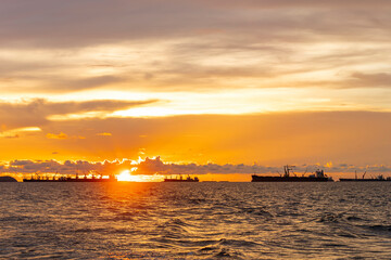 Bulk cargo ships for import export cargo anchored at the offshore sea horizon in the evening with a golden sunset.