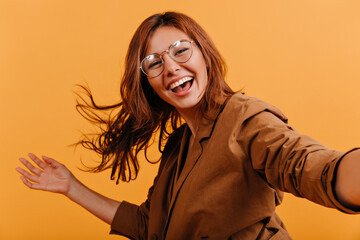 European model plays with red hair, posing for selfie. Snapshot of modern stylish girl in brown cotton jacket