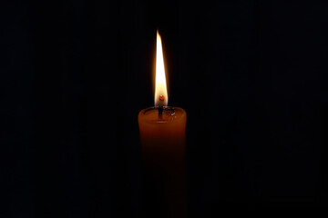 closeup of an isolated flame of a burning wax candle in the dark, black background