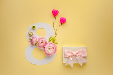Greeting Card International Women's Day on March 8th. Pink ranunculus decorates the number eight and gift box with bow on yellow background. Soft focus. Top view.