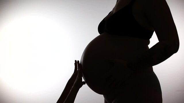 Silhouette of hands reaching for the belly of a pregnant woman. Illustration of the calmness of a mom next to the baby. Invisible love.