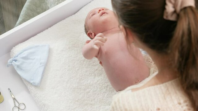 Slow motion of young mother putting ner little baby son on soft blanket on changing table. Concept of babies and newborn hygiene and healthcare. Caring parents with little children.