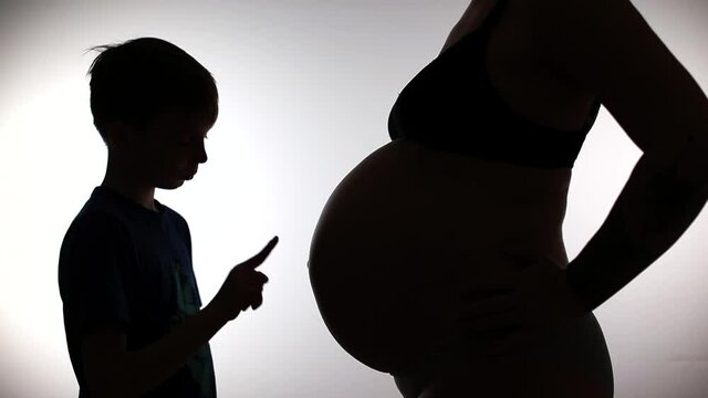Natural parenting touches mom's belly. Investigation of the secret connection of energy proximity. Silhouette of a teenager and a belly of a pregnant woman. 