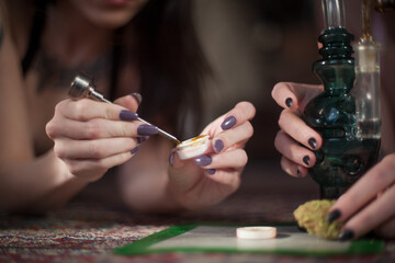 Women with nicely manicured fingernails use a titanium dabber tool to scoop concentrated cannabis...