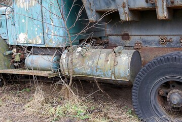 part of an old truck with a large gray gas tank and a black wheel in dry grass on the street