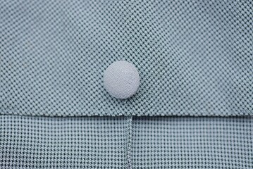 one small round white button on a gray garment fabric with a seam on the pocket