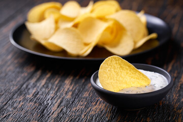 potato chips with white herb sauce, on a black wooden table with copy space for text.