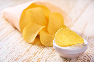 Potato chips in a takeaway paper cone with ketchup, on a white wooden table with copy space for text.