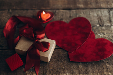 Happy Valentines day! Stylish gift box with red ribbon and red velvet hearts on rustic wood