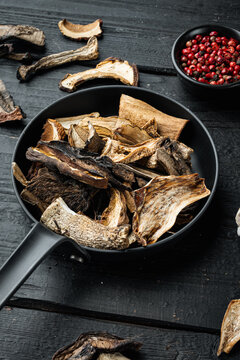 Mix of chopped wild dried mushrooms in cast iron frying pan, on black wooden table background