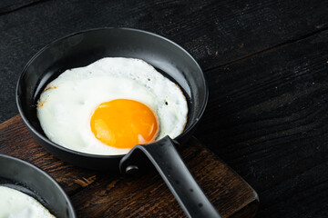 Fried eggs with bacon and vegetables in cast iron frying pan, on black wooden table background , with space for text  copyspace