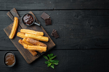 Traditional Spanish dessert churros with sugar and chocolate, on black wooden table background, top view flat lay with space for text, copyspace
