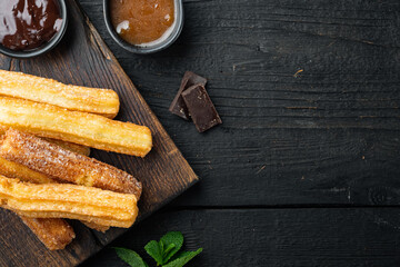 Traditional Spanish dessert churros with sugar and chocolate, on black wooden table background, top view flat lay with space for text, copyspace