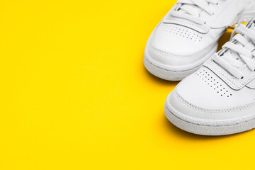 Pair of female stylish white casual sneakers on yellow background