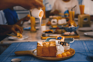 Hands are pouring sweetened condensed milk on honey toast.