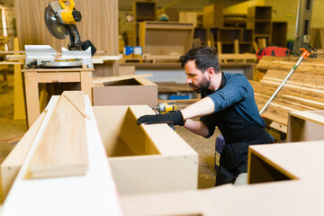 Handsome male worker using a power drill in a wood cabinet