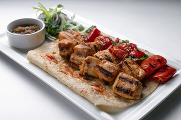 Chicken skewers on pita bread with marinated onion sauce and baked bell pepper on a white plate on a white plate