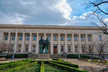 Obraz premium In front of Sts. Cyril and Methodius National Library with a statue and small park with dried trees and street on car. Bulgaria. Sofia. 06.01.2021.