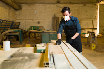 Handsome worker using a table saw to cut wood boards