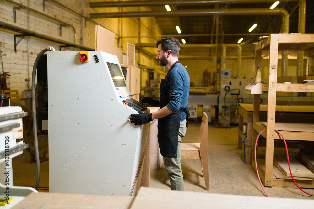 Wall mural Latin man controlling an industrial machine in workshop