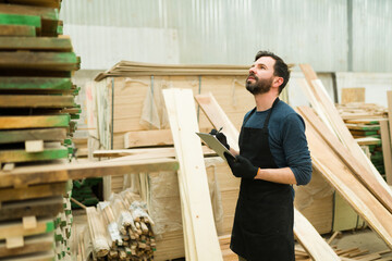 Latin man in his 30s looking up at a pile of wood boards