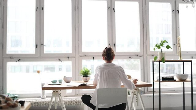 Rear view of young woman working on laptop in loft office
