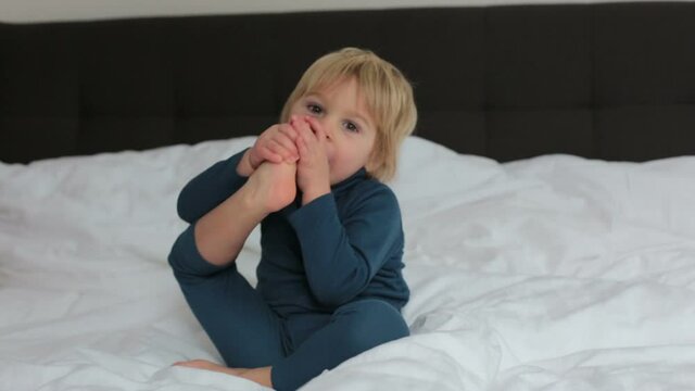 Cute blond toddler child, sucking his foot thumb, making funny faces, laughing