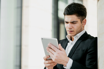 a serious manager is a business employee working in a business center in a bank. dark-haired European appearance. business suit and white shirt. copy space. holds a tablet and writes a message.