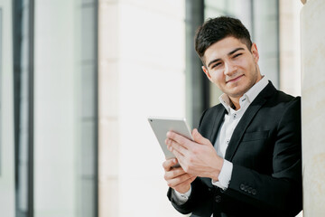 manager a business employee works in a business center in a bank. dark-haired European appearance. business suit and white shirt. copy space. holds a tablet and writes a message.