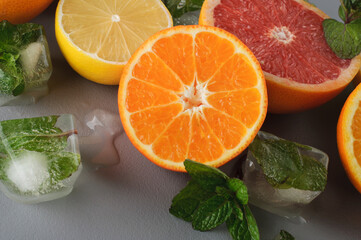 Half of lemon, grapefruit, tangerine with mint and ice cubes on a gray background. Preparation of cold drinks and juices. Citrus juice ingredients, food background