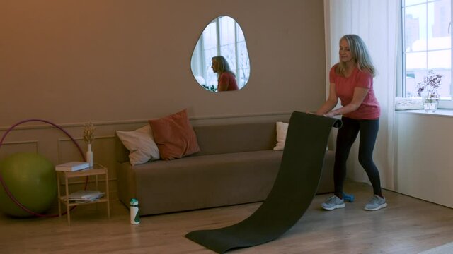 Athletic Attractive Middle Age Woman is rolling up the yoga mat at Home