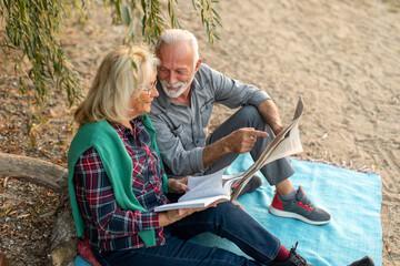 Portrait of an elderly couple sitting and reading a newspaper at the riverside beach.