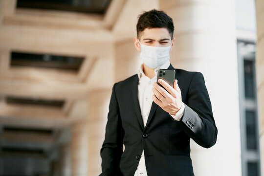 Wearing A Mask From The Coronavirus, The Manager Works In A Bank. The Man Is Dark-haired Of Italian Appearance. He Was Wearing A Black Business Suit And A White Shirt. Copy Space.